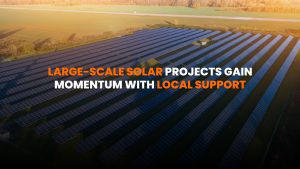 Community solar farm with panels installed on open land under blue sky, with town buildings in the background