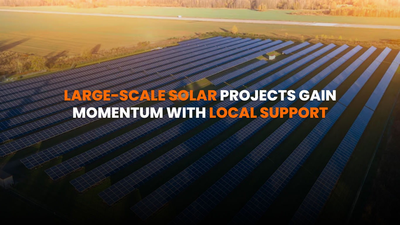 Community solar farm with panels installed on open land under blue sky, with town buildings in the background